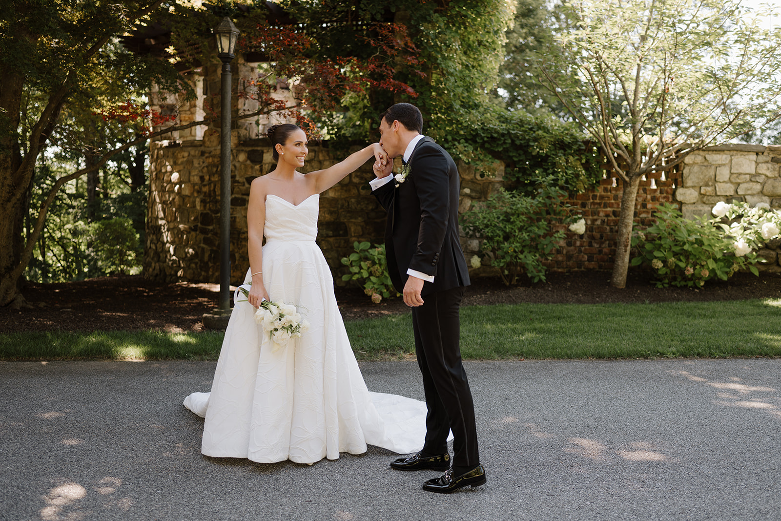 Groom kissing the bride's hand in front of the historic stone and brick walls of Le Chateau.